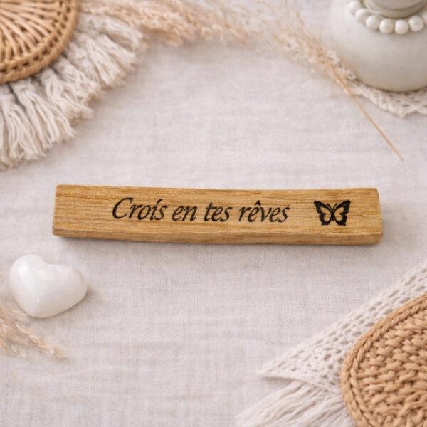 Bâton en Palo Santo gravé du message “Crois en tes rêves”, photographié dans une ambiance naturelle et bohème